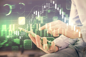 Double exposure of man's hands holding and using a digital device and forex graph drawing. Financial market concept.