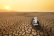 Young man paddle a boat at dry cracked earth with orange sky and hot weather of the sun. Metaphor Climate change, Drought and water crisis concept.