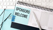 SPONSORS WELCOME text on blue sticker on planning and keyboard,blue background