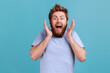 © khosrork - Portrait of pleasantly surprised glad bearded man smiles broadly shocked to receive unexpected news, looking at camera, expressing excitement. Indoor studio shot isolated on blue background.