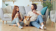© alex_marina - Happy Young Married Couple Sitting on the Floor Near a Couch and Clinking Glasses With Wine, celebrating new house purchase, successful mortgage investment. Cute Dog Sitting Between Married Couple.