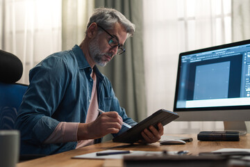 mature man architect working on computer at desk indoors in office.