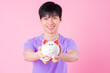 © Timeimage - Young Asian man holding piggy bank on pink background