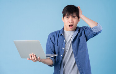 Young Asian man using laptop on blue background