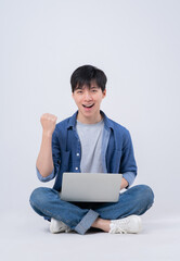 Wall Mural - Young Asian man sitting and using laptop on white background