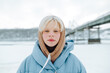 © bodnarphoto - beautiful girl with white eyebrows and hair in a blue jacket stands in the winter outdoors in the cold and looks at the camera, close-up portrait