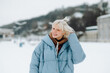 © bodnarphoto - Positive blonde girl with blond hair stands on a snowy street in a bag and looks at the camera with a smile on his face.