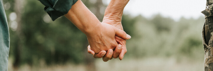 happy senior couple holding hands. hands of man and woman hold each other. romance and love and support in elderly family. faceless husband and wife travel together in nature. countryside life. banner