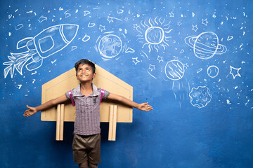 happy kid with cardboard rocket on back with space, universe and planets doodle drawing on wall - co