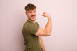 young cool man feeling happy, satisfied and powerful, flexing fit and muscular biceps, looking strong after the gym