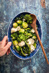 Top down view of a hand holding a dish of steamed cruciferous vegetables.