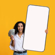 Cashback concept. Shocked woman holding huge smartphone with blank screen and cash money dollar banknotes, mockup