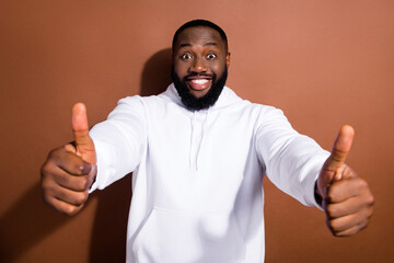 Wall Mural - Photo of funny pretty guy dressed white sweatshirt showing two thumbs up isolated brown color background