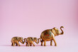 Golden elephant figurines on a pink background. A family of Indian elephants. Sacred animals in India. Luck and stability in the house by elephant's energy