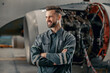 Joyful man aircraft maintenance technician looking away and smiling while keeping arms crossed
