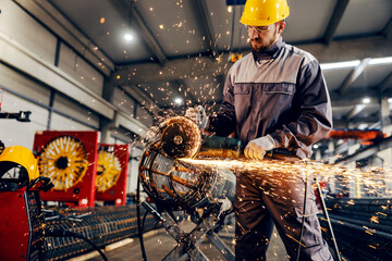 A metal and iron factory worker processing metal construction with grinder.