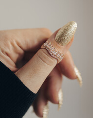 Wall Mural - Female hand with glittered golden nail and with beautiful stylish ring on finger. Close up photo.