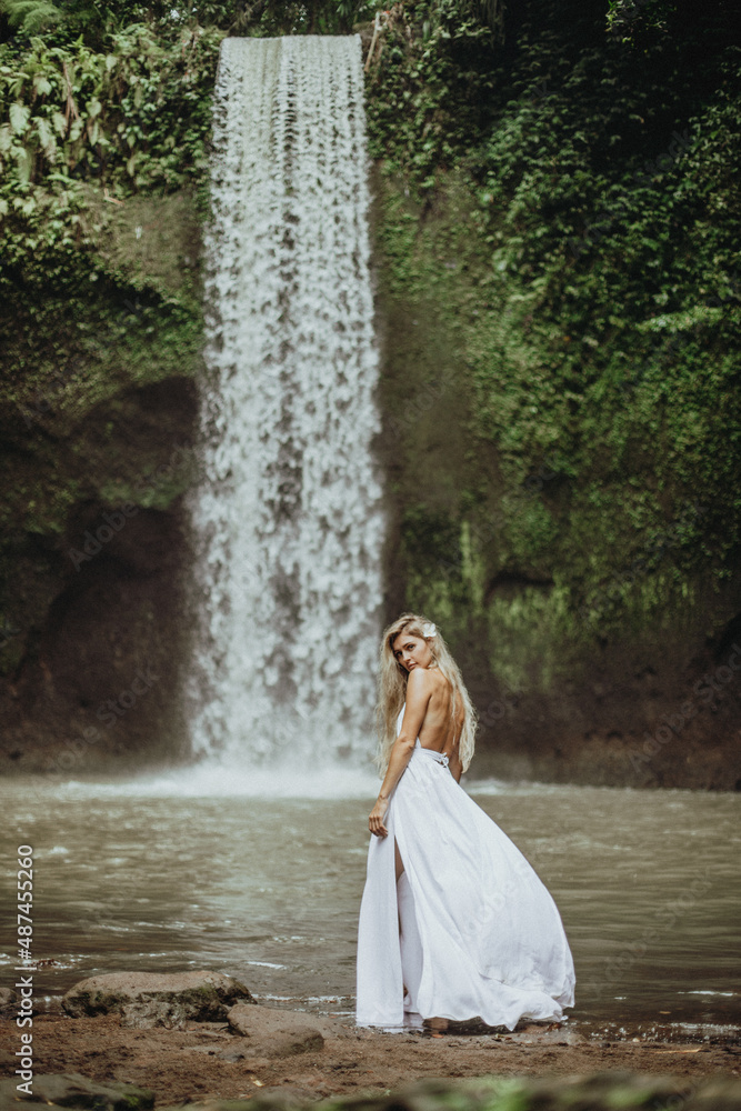 a young beautiful girl at a waterfall in a white wedding dress, a girl in  the tropics against the backdrop of a waterfall, young beautiful blonde in  a white dress Stock-foto |