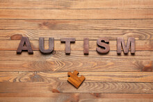 Word AUTISM And Puzzle Piece On Wooden Background