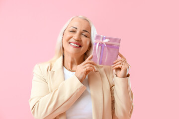 Wall Mural - Smiling mature woman with closed eyes holding gift box on pink background. International Women's Day celebration