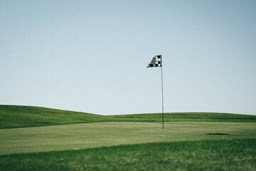 Canvas Print - Golf flagstick waving in a green field with a light blue sky in the background