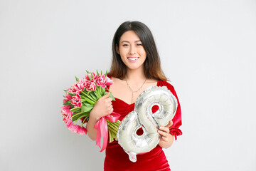 Beautiful young Asian woman with bouquet of flowers and balloon in shape of figure 8 on light background. International Women's Day celebration