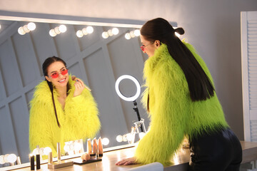 Wall Mural - Young woman applying make up near illuminated mirror indoors