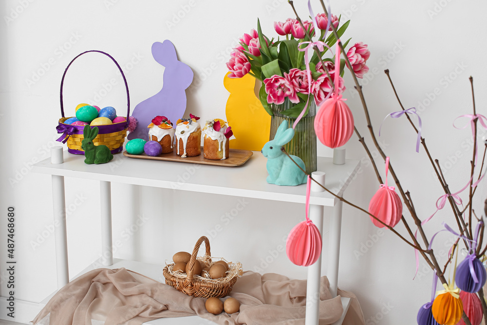Easter cakes, eggs and decor on shelf unit near white wall