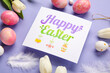 © Pixel-Shot - Beautiful Easter composition with greeting card, painted eggs and flowers on purple background, closeup