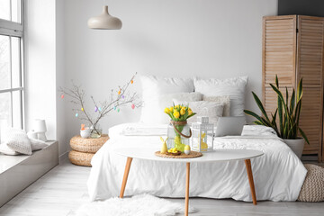 Vase with tulips, nest with Easter eggs and decor on table in light room interior