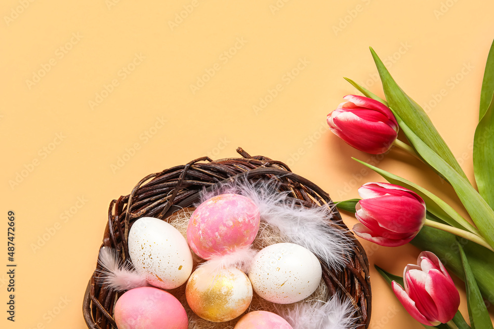 Nest with painted Easter eggs, feathers and flowers on color background