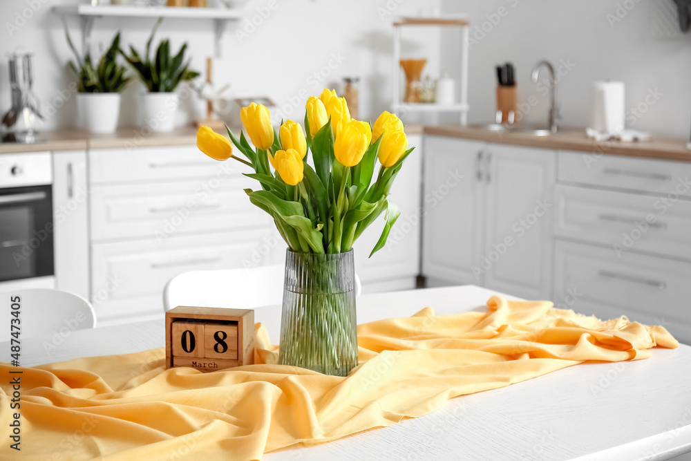 Cube calendar and vase with bouquet of tulips on dining table. International Women's Day celebration