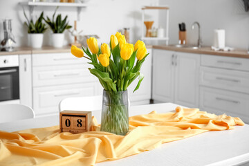 Cube calendar and vase with bouquet of tulips on dining table. International Women's Day celebration