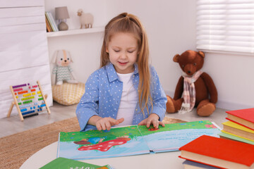 Canvas Print - Cute little girl reading book at table in room