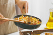 Woman with frying pan of cajun chicken pasta on table in kitchen