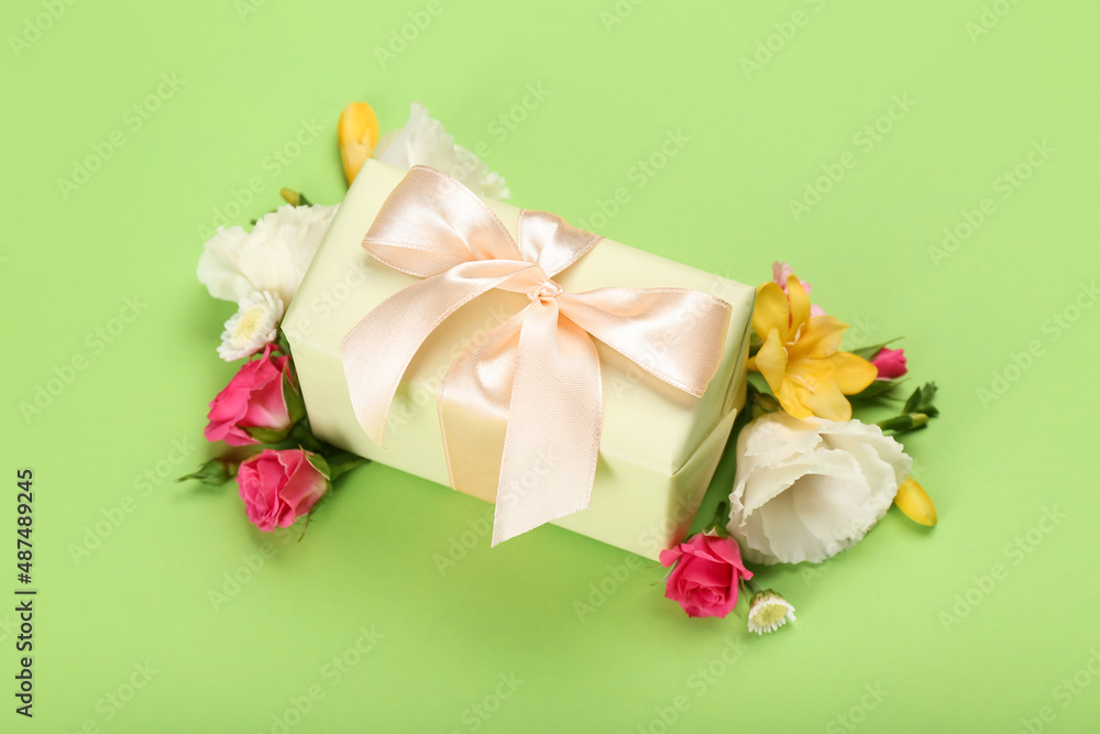 Beautiful spring composition with flowers and gift box on green background
