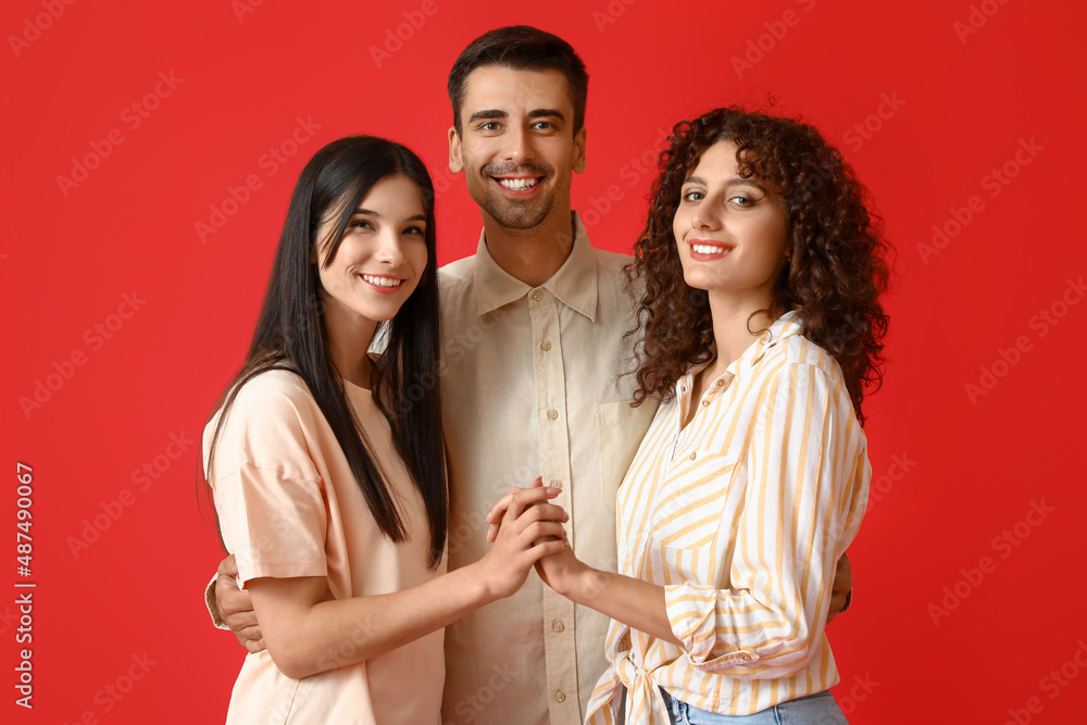 Man and two beautiful women on color background. Polyamory concept