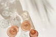 © yrabota - Set colored glasses from transparent and beige glass with beautiful shadows from palm leaf at sunlight, summer drink for events, white wine, water in trend glasses, aesthetic top view