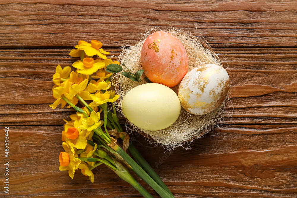 Nest with painted Easter eggs and flowers on wooden background
