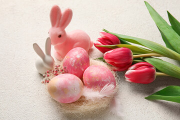 Nest with painted Easter eggs, bunnies and flowers on light background