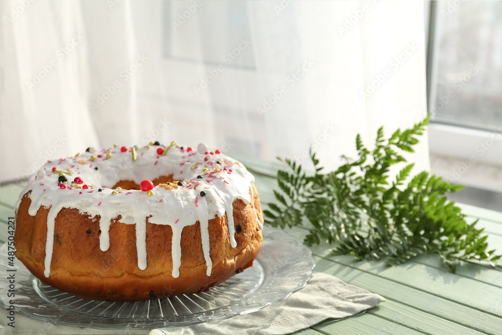 Plate with tasty Easter cake and green branch on wooden table