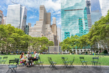 New York City People Lifestyle. Group Of Tourists Eating Lunch Sitting At Public Chairs And Tables In Bryant Park, Popular Destination In NYC, USA Summer Travel Destination.