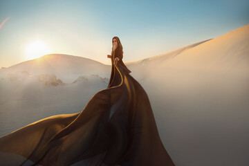 mystery arabic woman in black long dress stands in desert long train silk fabric fly flytter in wind