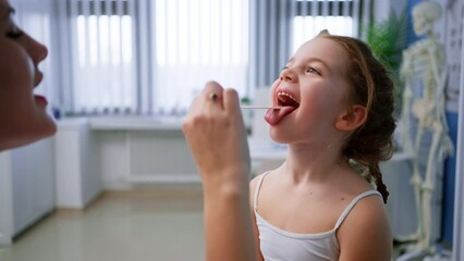 Wall Mural - young male doctor checking little girl's throat in his office.