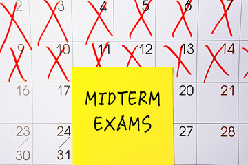 The phrase Midterm exams written on a yellow sticky note posted on a calendar or planner page as a reminder. Closeup of a personal agenda
