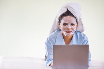 Wall Mural - Portrait of young woman applying facial mask on her face during using laptop on bedroom