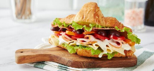 Wall Mural - Croissant sandwich with cheese, ham, lettuce, tomatoes, olives and delicious sauce on wooden board.