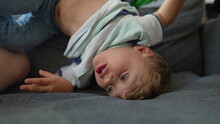 Bored Little Boy At Home In Upside Down On Sofa Child Playing Alone