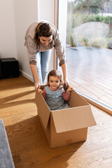 Poster - family, hygge and people concept - happy mother and little daughter sitting in box playing at home