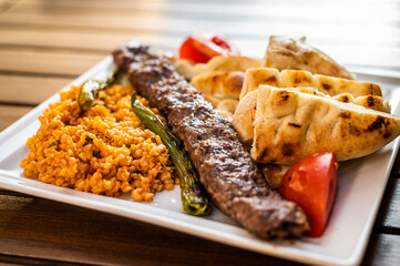 Turkish Adana kebab on a plate with marinated peppers,  bread and rice pilaf. Top view